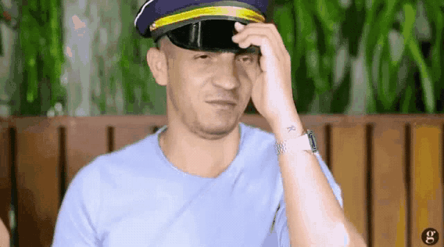 a man wearing a military hat is sitting on a bench and covering his face with his hand .