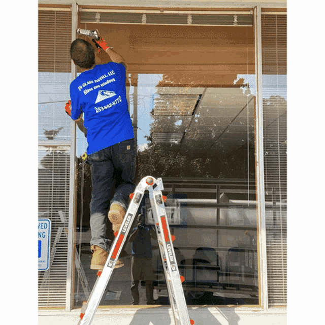 a man standing on a ladder wearing a blue shirt that says glass install llc on it