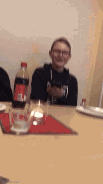 a boy sits at a table with a bottle of coca cola in the background