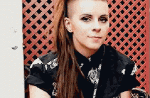 a woman with dreadlocks and a shaved head is sitting in front of a red lattice wall .