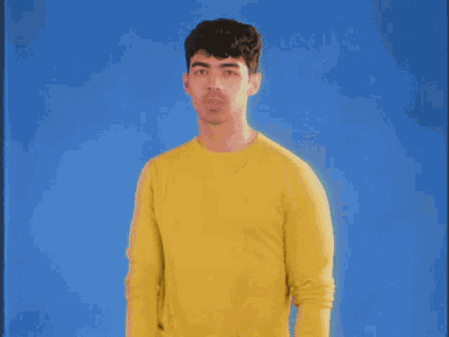 a man wearing a yellow sweater is standing in front of a blue background .