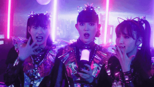 a group of three girls are standing next to each other in a dark room with neon lights .