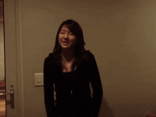 a woman in a black shirt is smiling in front of a wall with a light switch on it