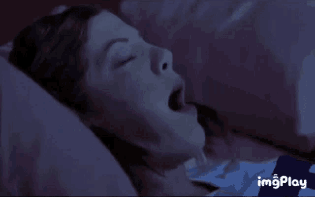 a woman is yawning while laying in bed at night .