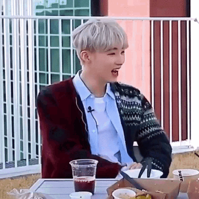 a young man is sitting at a table with a box of food and a drink .