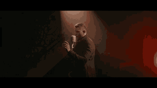 a man in a black coat is singing into a microphone .