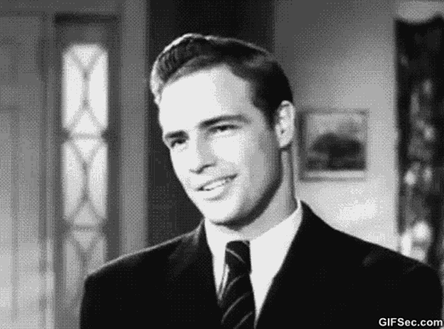 a black and white photo of a man wearing a suit and tie smiling .