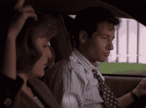 a man and a woman are sitting in a car . the man is wearing a tie and a striped shirt .