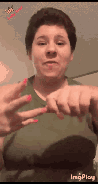 a woman in a green tank top with pink nails is making a gesture with her hands ..