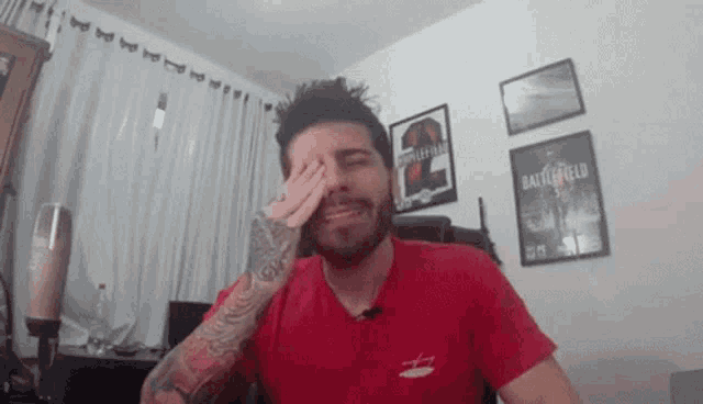 a man with a beard wearing a red shirt is covering his eyes .