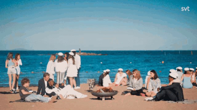 a group of people sit around a fire pit on a beach with the svt logo in the corner