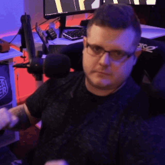 a man wearing glasses is sitting in front of a microphone in front of an acer computer