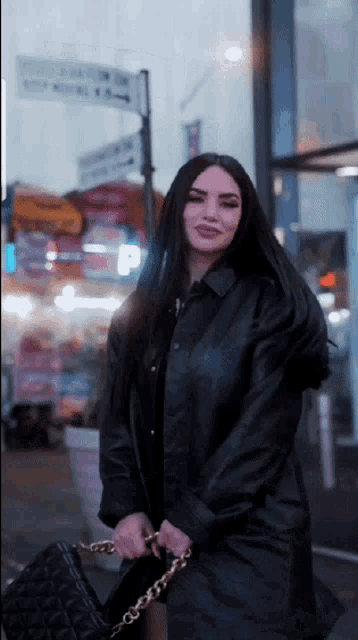 a woman in a black leather coat is holding a black bag