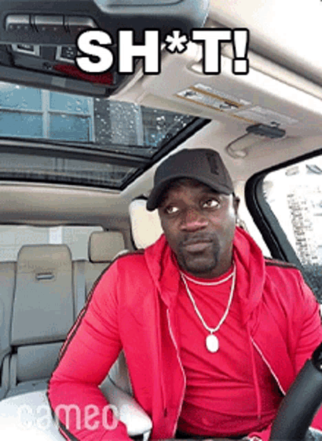 a man in a red jacket is sitting in the driver 's seat of a car with a caption that says shot
