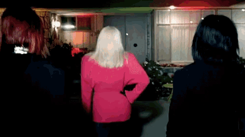 a woman in a pink sweater is standing in a dark room .