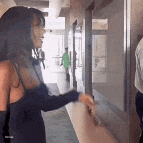 a woman in a black dress is standing in a hallway talking to a man in a green shirt .