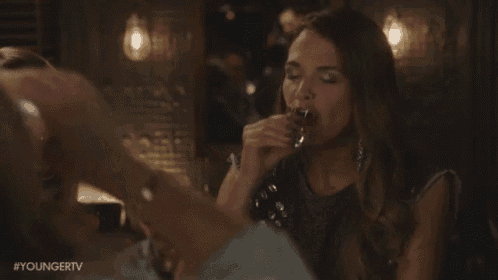 a woman is drinking a shot of liquor from a glass .
