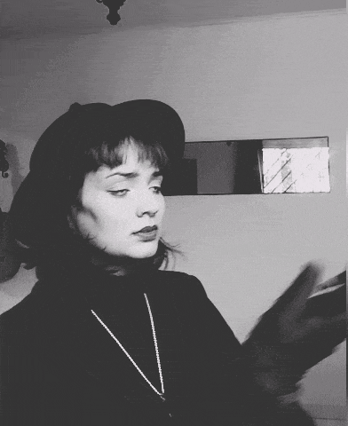 a woman wearing a hat and a necklace is standing in front of a mirror