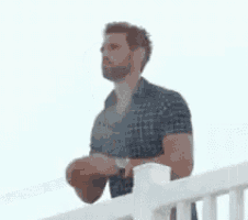 a man is covering his face while standing on a railing .