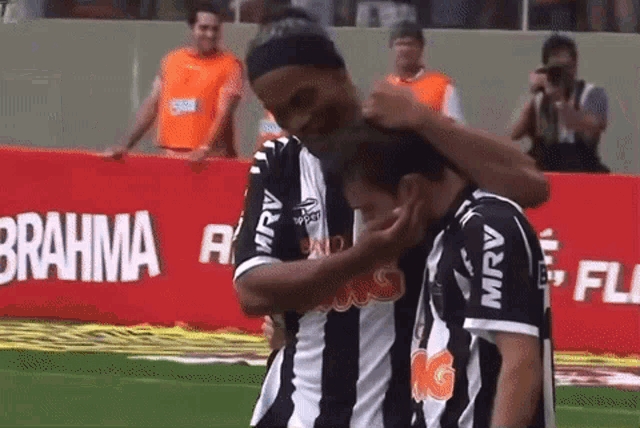 a soccer player is hugging another player in front of a brahma banner