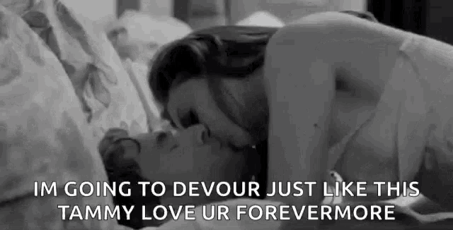 a black and white photo of a man and woman kissing on a bed with a caption .