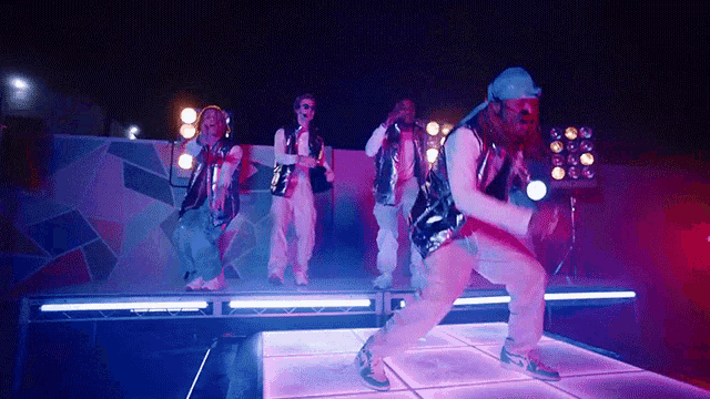a group of people are dancing on a stage with purple lights behind them