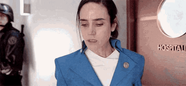 a woman in a blue suit is standing in front of a door that says hospital .