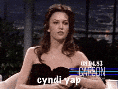 a woman in a black dress is sitting in front of a sign that says cyndi yap on it