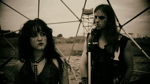 a man singing into a microphone next to a woman with black paint on her face