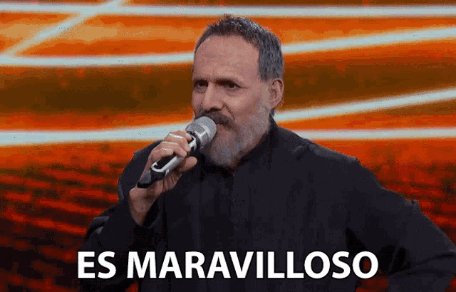 a man with a beard is singing into a microphone with the words es maravilloso below him