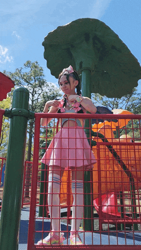 a girl in a pink dress and white socks stands in a playground