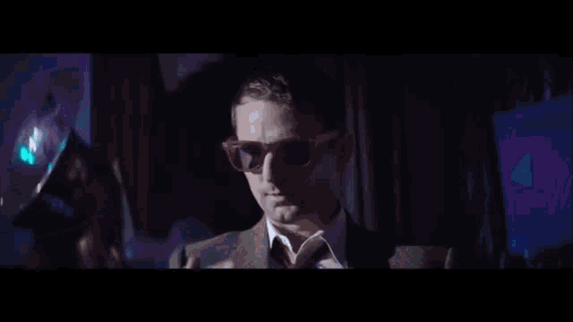 a man in a suit and tie is wearing sunglasses and touching a glowing hand .