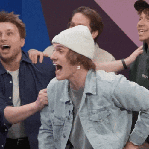 a man wearing a white beanie and a denim jacket is surrounded by other men