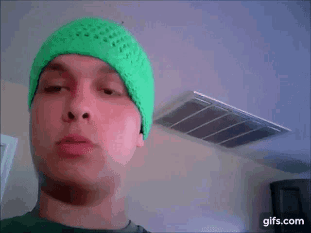 a man is wearing a green beanie and making a funny face .