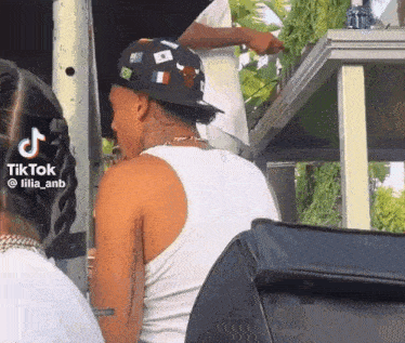 a man wearing a hat and a tank top is sitting next to a woman .