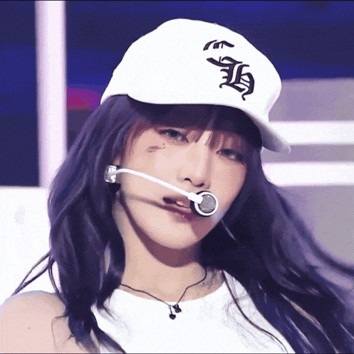 a woman with purple hair wears a white hat with the letter h on the front