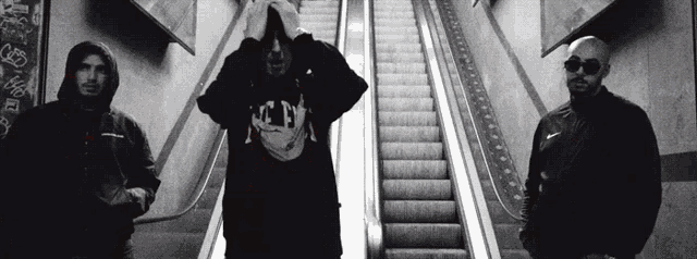 three men are standing on an escalator with one wearing a shirt that says tn