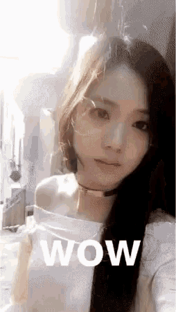 a woman with long black hair is taking a selfie with the word wow written on her face .