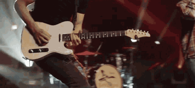a man is playing a guitar on stage with a drum set in the background