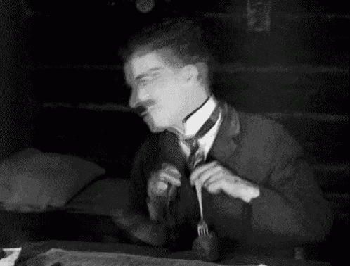 a black and white photo of a man sitting at a table holding a fork and spoon .
