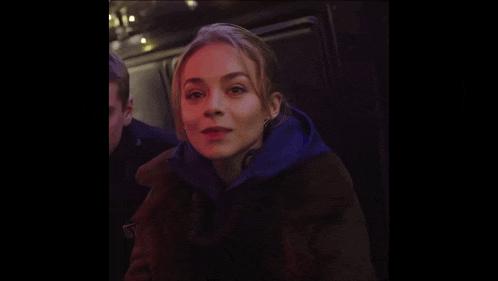 a woman wearing a fur coat and a blue hoodie has a sticker on her jacket that says ' fbi '