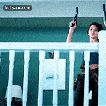 a woman is holding a gun over a balcony railing while another woman watches .