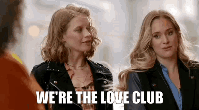 two women are standing next to each other and the words we 're the love club are on the screen .