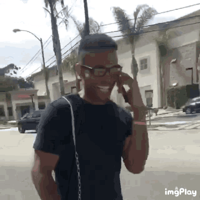 a man wearing glasses and a black shirt is smiling while talking on a cell phone ..