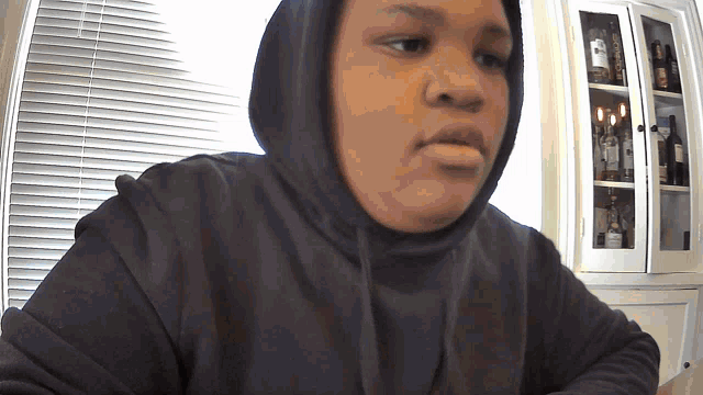 a person wearing a black hoodie is sitting in front of a window with blinds