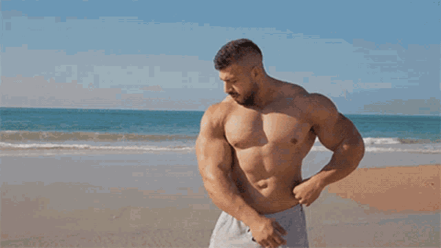 a shirtless man flexes his muscles on a beach