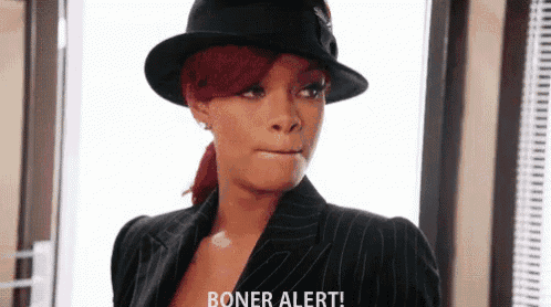 a woman wearing a hat and a suit is standing in front of a window and making a funny face .