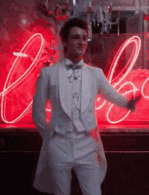 a man in a white tuxedo is dancing in front of a neon sign .