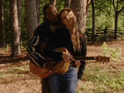a man holding a guitar while a woman looks on while wearing a sweatshirt that says stadium