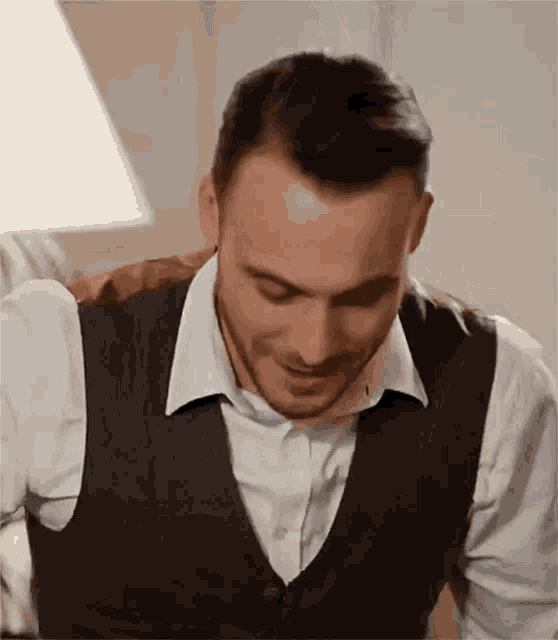 a man wearing a vest and a white shirt is laughing .